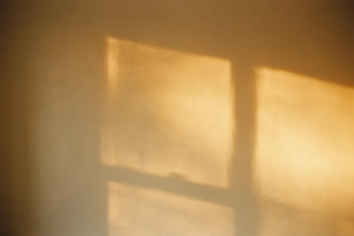 Warm morning sunlight breaking across a pale plaster wall in a soft expanding gradient.