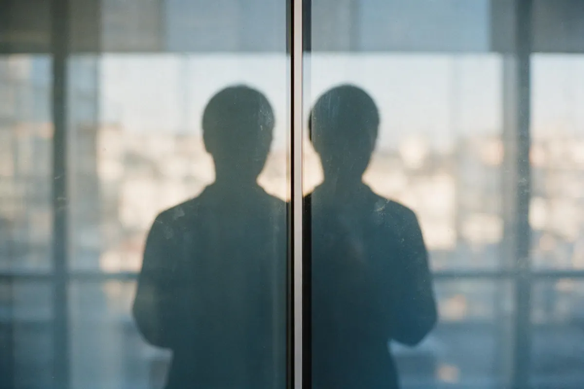 A silhouette reflected and doubled in two adjacent panes of tinted office glass.