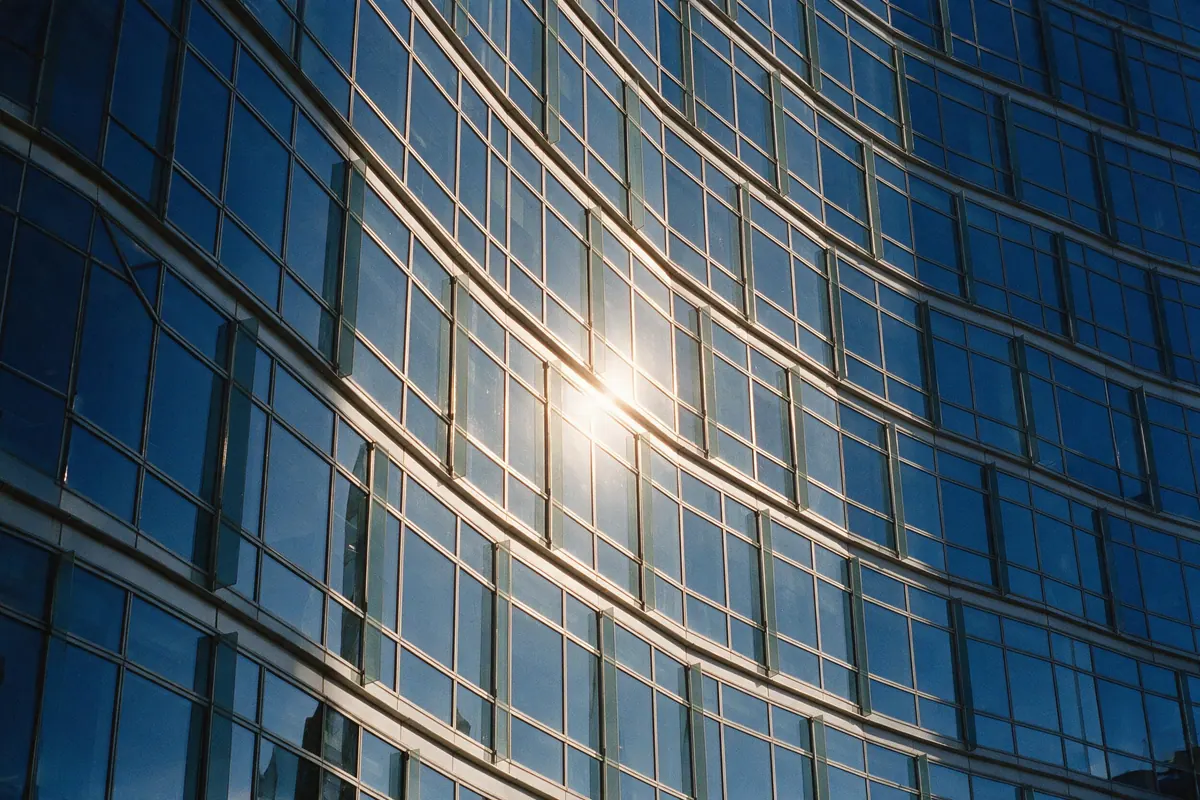 A curved glass and steel building facade catching low morning sun in clean repeating geometry.